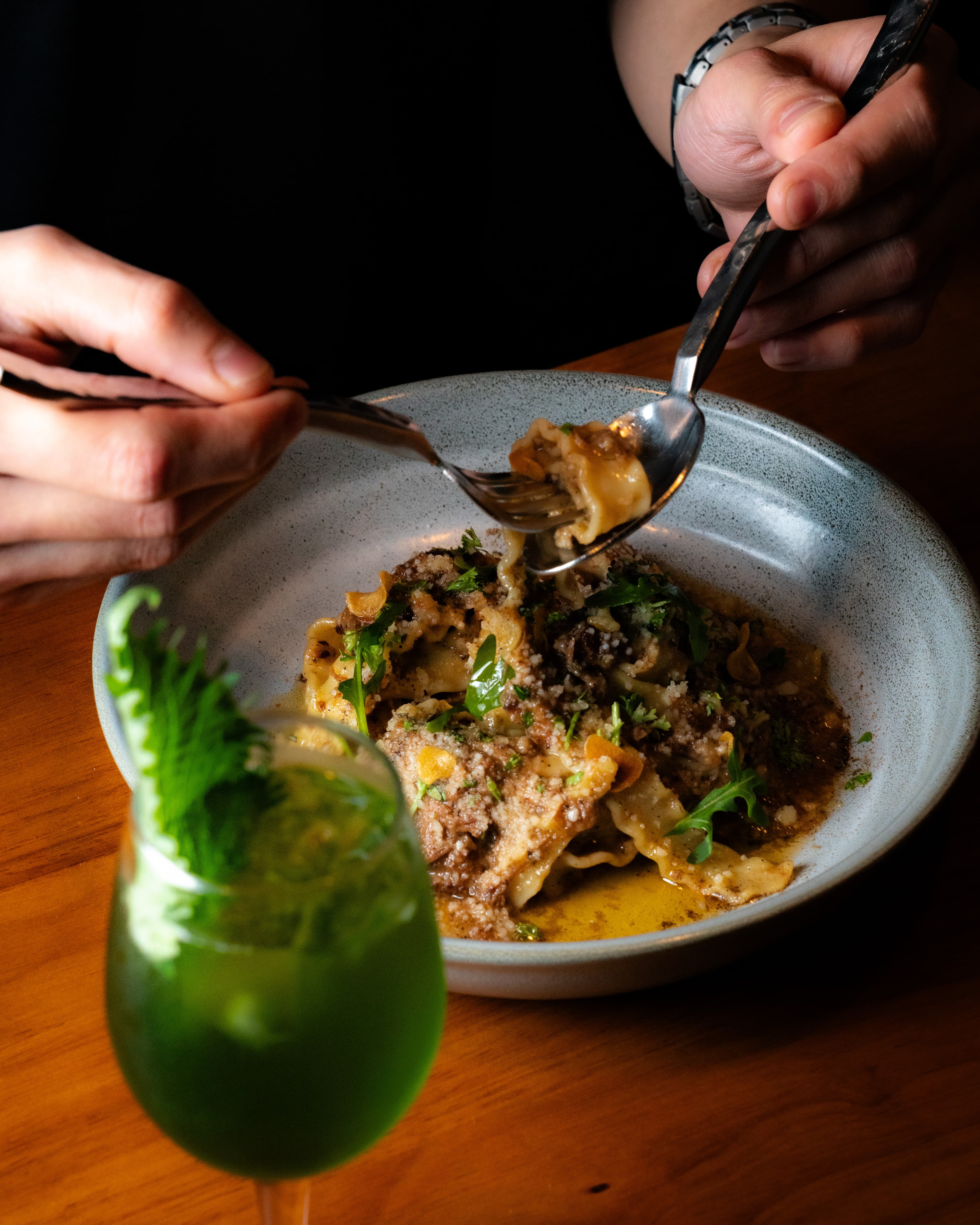 Man eating wagyu ragu pasta with a green cocktail on To;asta table.